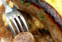 A white bowl containing yukon Gold Mashed potatoes, onion ale gravy, and two sausages (bangers). A sausage is cut open revealing the inside