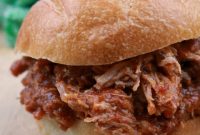 A Portuguese Pulled Pork Sandwich, Cacoila, on a cutting board with a green towel in the background.